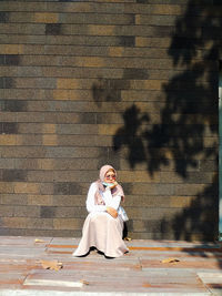 Full length of woman sitting against wall