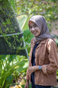 Portrait of a beautiful woman wearing a modern hijab on the side of the greenhouse with sweet smile