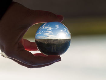 Close-up of hand holding crystal ball against sky