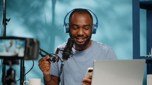 Happy young man using smart phone while blogging with camera