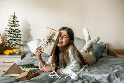 Portrait of smiling girl holding envelope sitting on bed at home