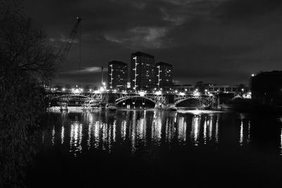 Illuminated buildings by river against sky in city at night