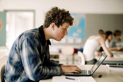 Side view of teenage boy using laptop while sitting in classroom