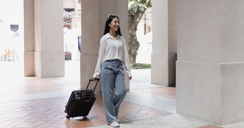 Full length of young woman with suitcase walking in street