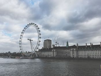 Ferris wheel in city against cloudy sky