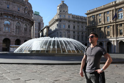 Young man standing against fountain at piazza de ferrari