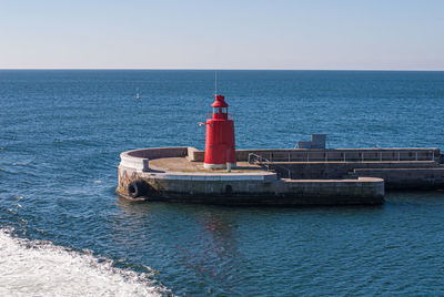 Lighthouse by sea against clear sky