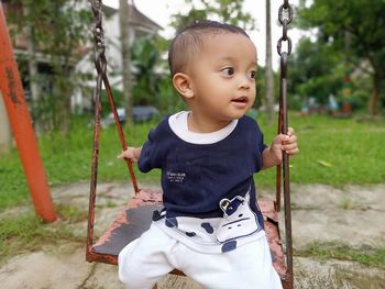 Cute baby boy sitting on swing at playground