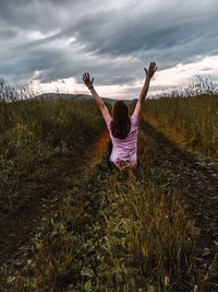 Rear view of woman with arms raised on field against sky