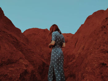 Rear view of woman standing on rock against sky