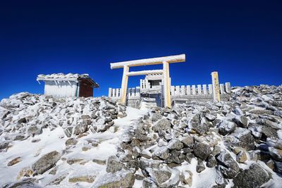 Low angle view of snow covered rocks against clear blue sky