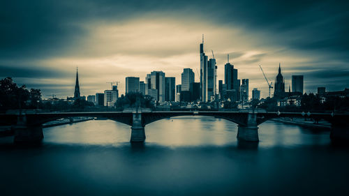 Bridge over river by buildings in city against sky