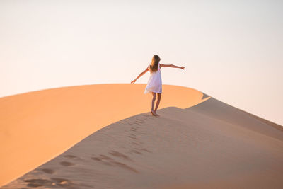 Full length of woman standing on sand dune against clear sky