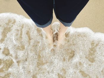 Low section of woman standing in shallow water at beach