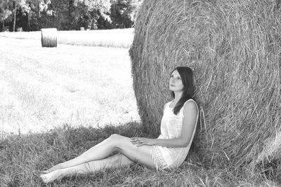 Thoughtful woman leaning on hay bale while sitting at farm field