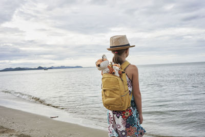 Girl with stuffed toys in bag looking at sea