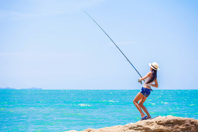 Woman fishing while standing on rock against sky