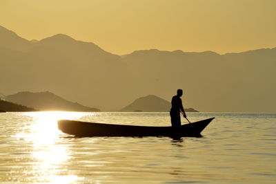 Silhouette man in boat on lake against sky during sunset