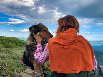 Rear view of woman with dog sitting on mountain against sky