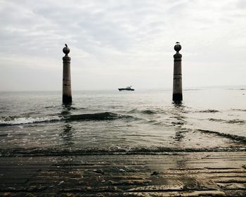 Low angle view of columns in sea against cloudy sky