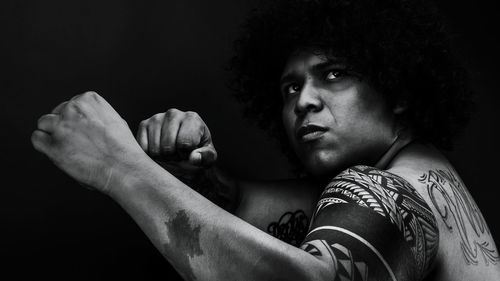 Serious man with tattoos in boxing stance against black background