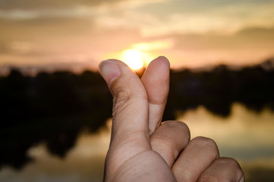 Close-up of person hand against sky during sunset