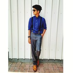 Full length of young man wearing suspenders while standing against wall