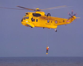 Man hanging from rescue helicopter flying over sea