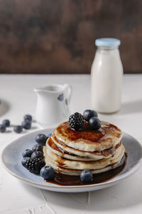 Pancakes topped with syrup and berries, with a bottle of milk in the background