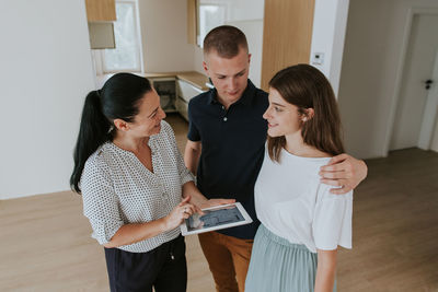 Woman with digital tablet talking with couple standing on floor at home