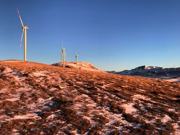 Windmills on landscape against clear blue sky