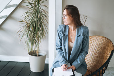 Young woman with long hair in suit with notes in hands sitting on chair in modern office