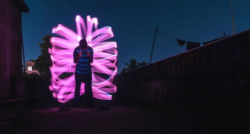 Rear view of woman standing on illuminated street against sky at night