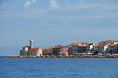 Sea by buildings in city against sky