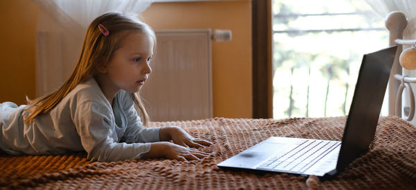 Child watching cartoons on laptop. serious kid with technology at home on bed spending time on-line