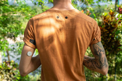 Midsection of shirtless man standing against trees