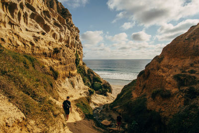 Rear view of people standing amidst cliffs by sea against sky