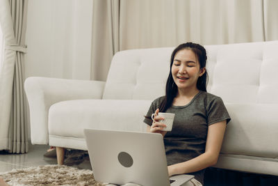 Portrait of smiling woman using phone while sitting on sofa