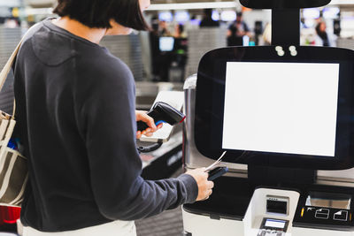 Woman passenger self check in scanning qr code boarding pass at airport with scanner.
