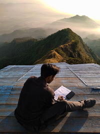 Man sitting on book by mountains against sky