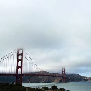 View of suspension bridge over river against cloudy sky