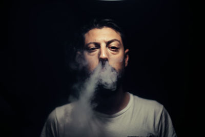 Close-up of young man smoking against black background