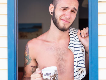 Close-up portrait of man winking while having coffee standing at doorway