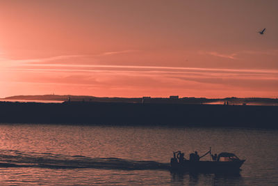 Silhouette men in sea against sky during sunset