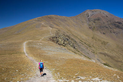 Rear view of woman walking on mountain showing all long path to go against blue sky