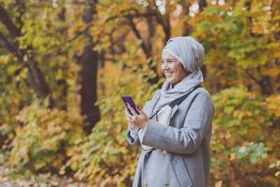 Young woman using phone while standing on tree