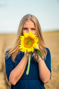 Portrait of woman with yellow flower against sky