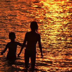 Silhouette siblings in sea at sunset