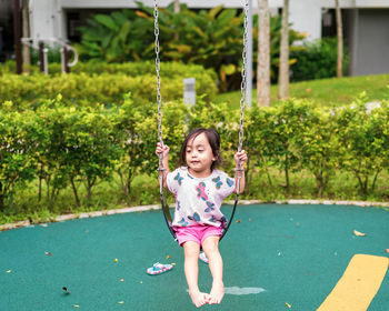 Cute small child smiling while playing swing by herself at the kid's playground, 