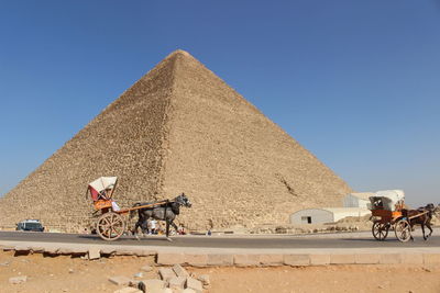 People riding horse cart in desert against clear sky